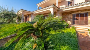 A two-story house with a stone facade, a balcony, and a lush garden with palm trees. - Residenza Lu Fraili (San Teodoro)
