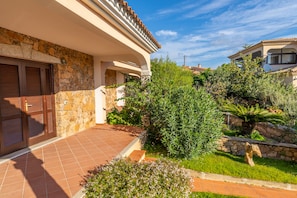 Una casa con fachada de piedra, un patio adoquinado y un jardín exuberante con diversas plantas y una palmera.