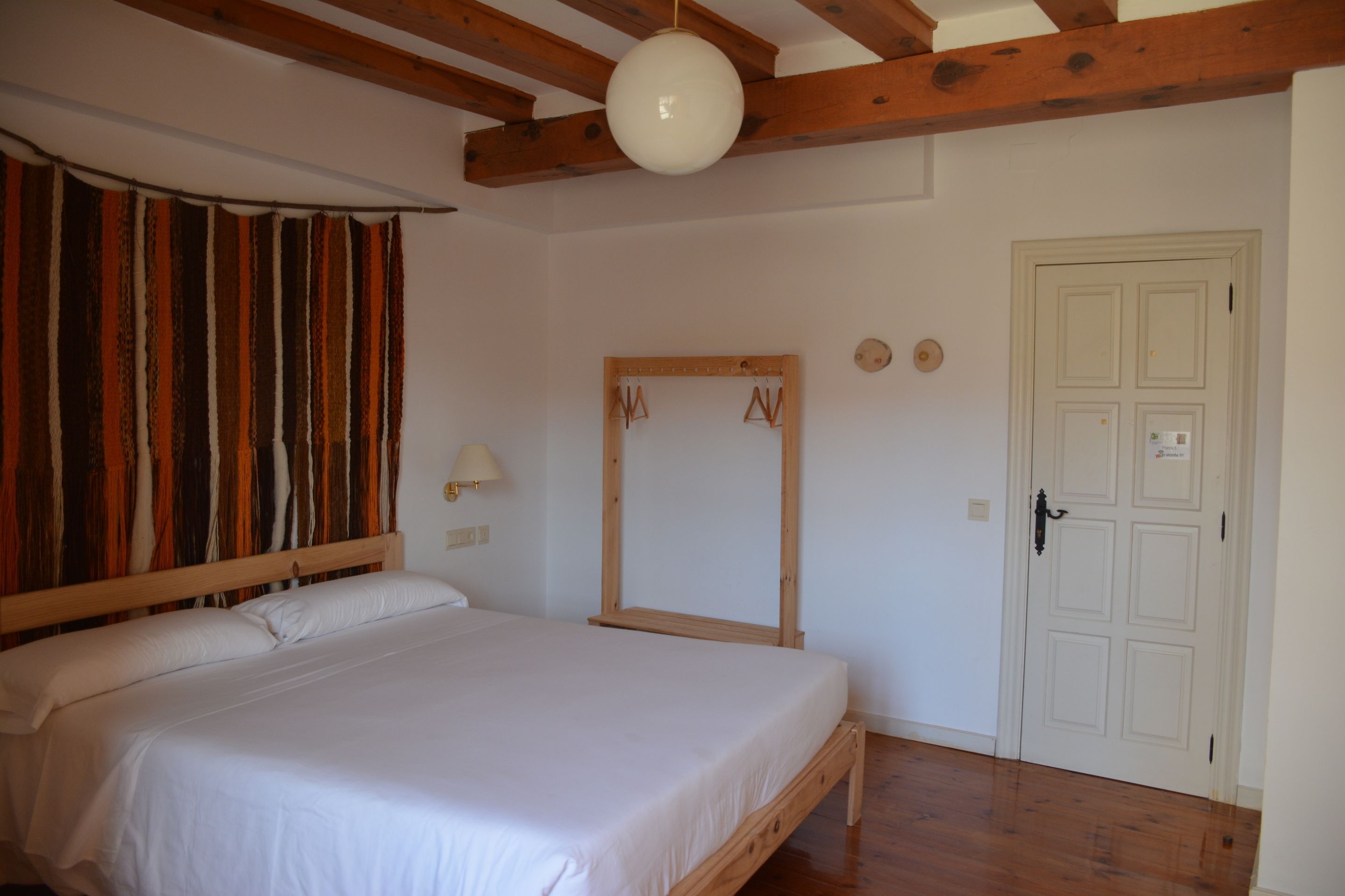 Un dormitorio con cama de madera, espejo, puerta y pared con cortina.