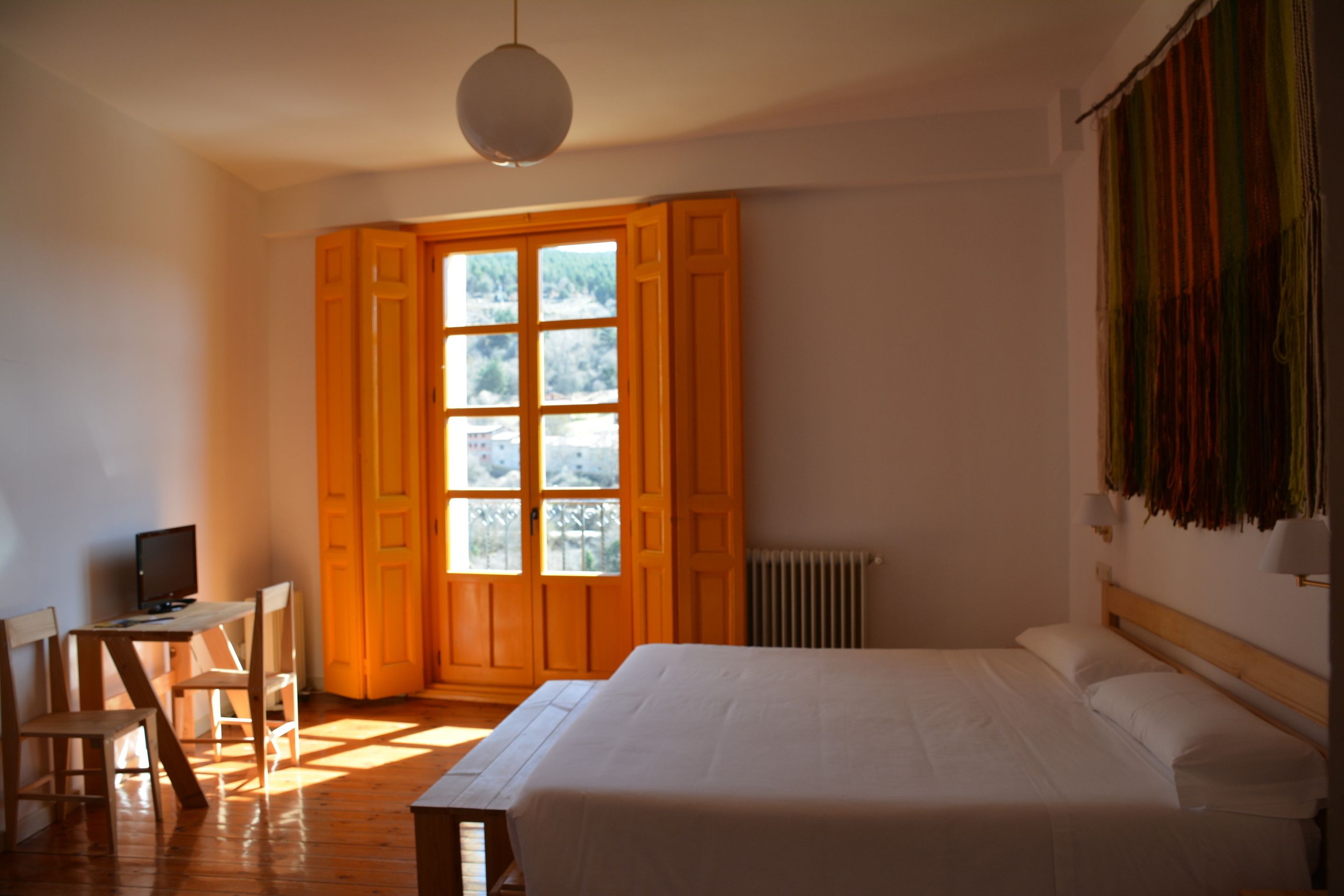 Un dormitorio con una cama, un escritorio con computadora y una ventana con cortinas.