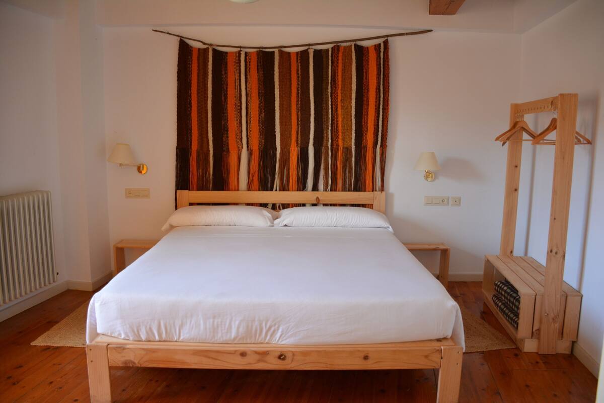 A bedroom with a wooden bed, a striped curtain, bedside lamps, and a wooden coat rack.