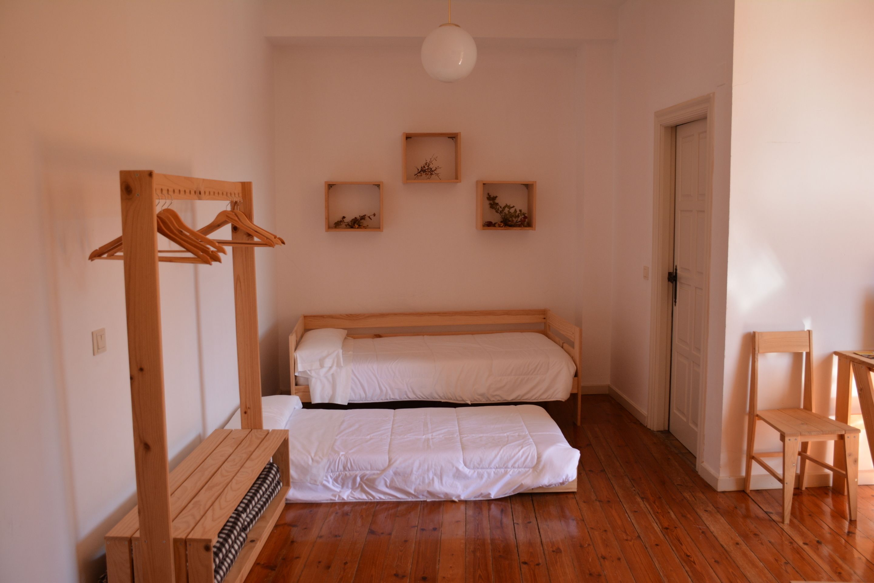 Un dormitorio con dos camas, una silla de madera, un estante de madera y marcos de cuadros colgados en la pared.