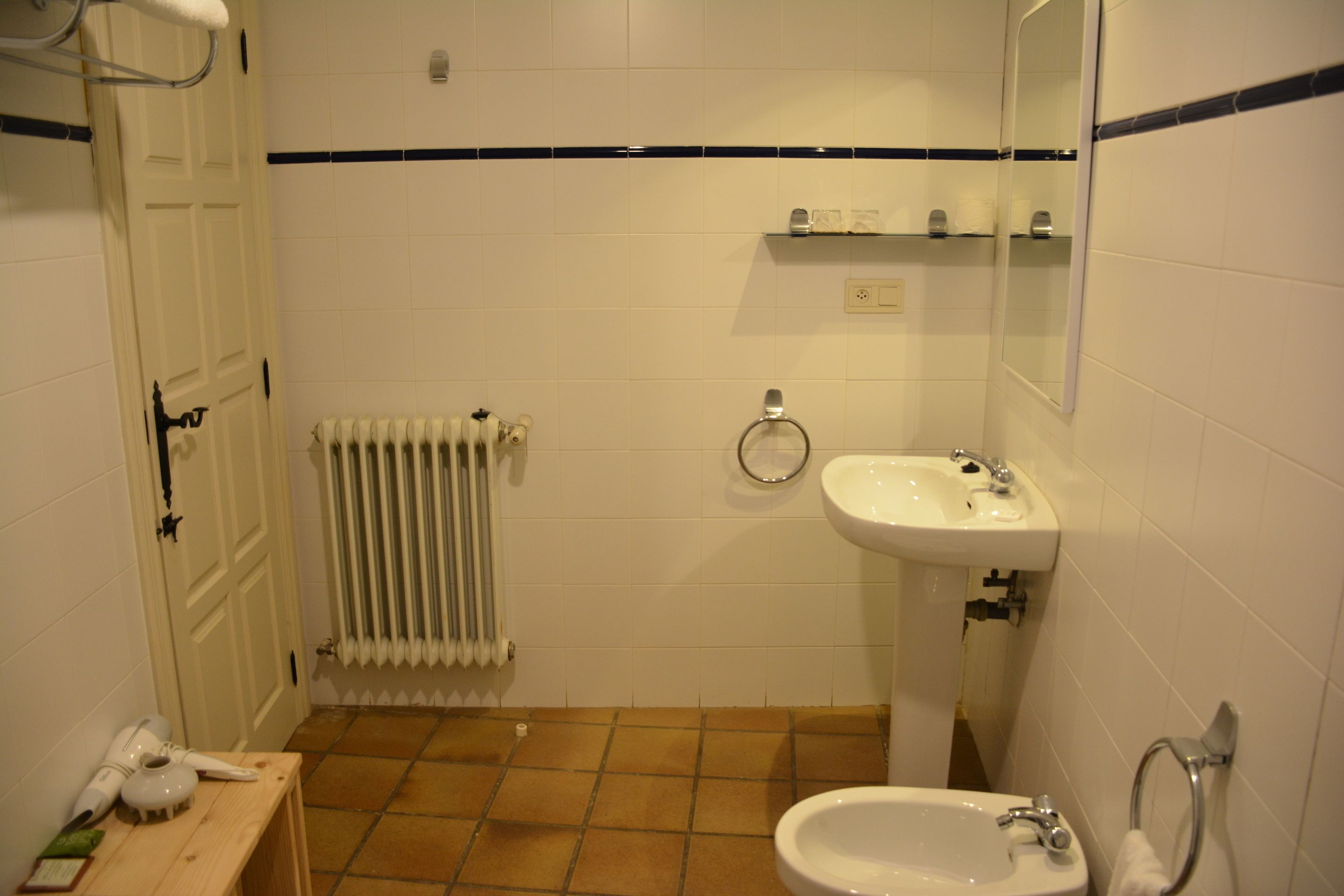 Un baño con un lavabo blanco, un inodoro, un radiador y un estante de madera.