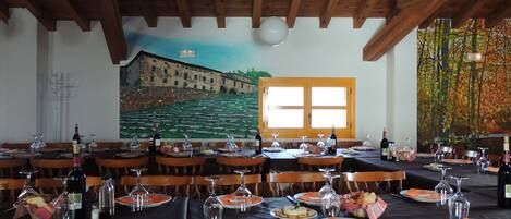 Zona pranzo con tavoli apparecchiati per diversi ospiti, travi a vista al soffitto e un affresco raffigurante un edificio.