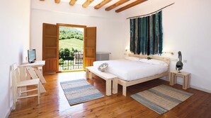 Un dormitorio con techo de madera, una cama, un escritorio y vista a un paisaje verde a través de una puerta abierta.