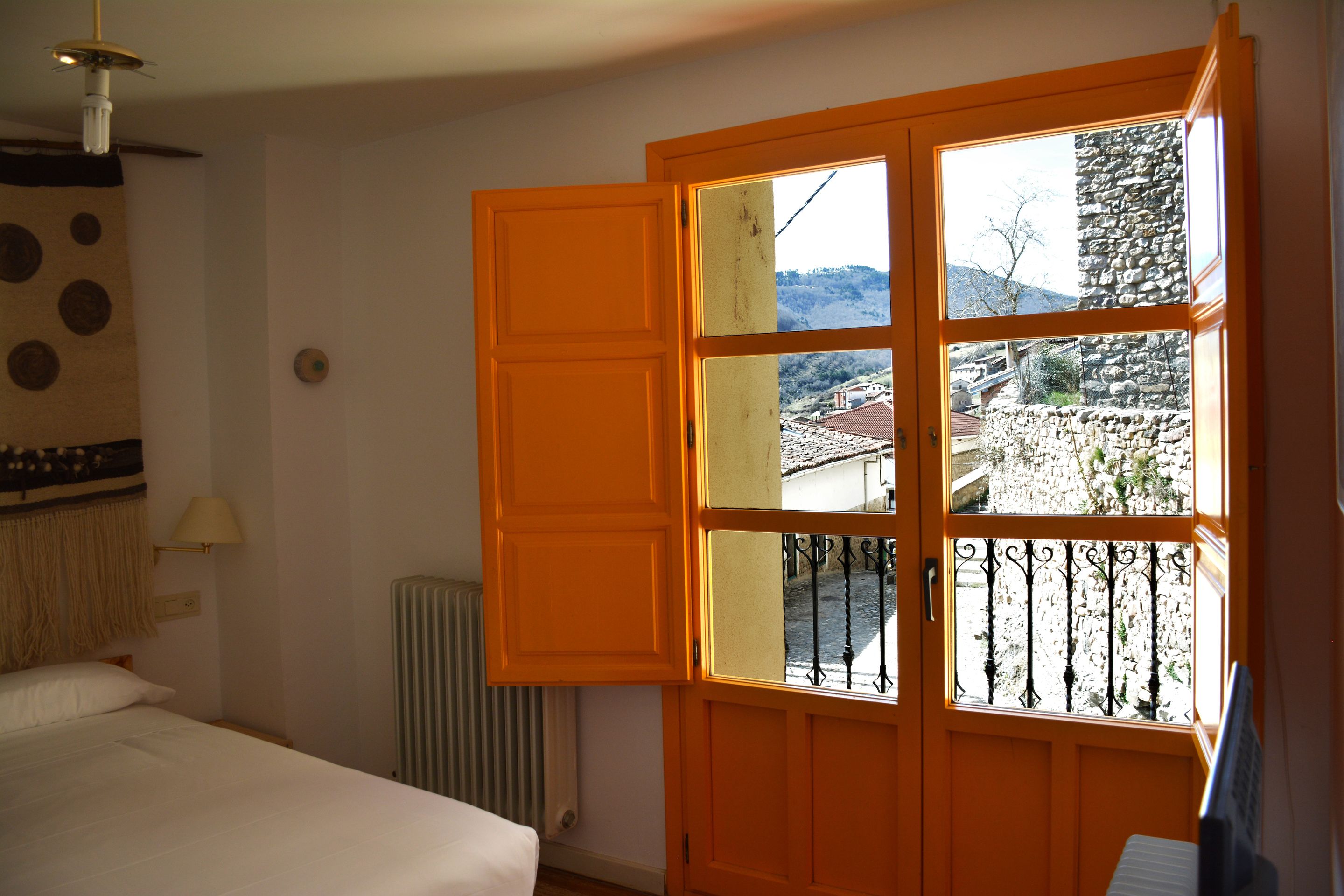 Une pièce avec un lit, un radiateur et une fenêtre donnant sur un mur de pierre et un immeuble.