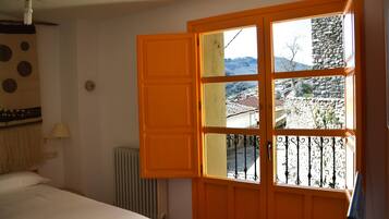 Une pièce avec un lit, un radiateur et une fenêtre donnant sur un mur de pierre et un immeuble.