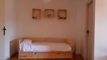 A small, single-bed room with wooden flooring, a white door, and three wall-mounted picture frames.