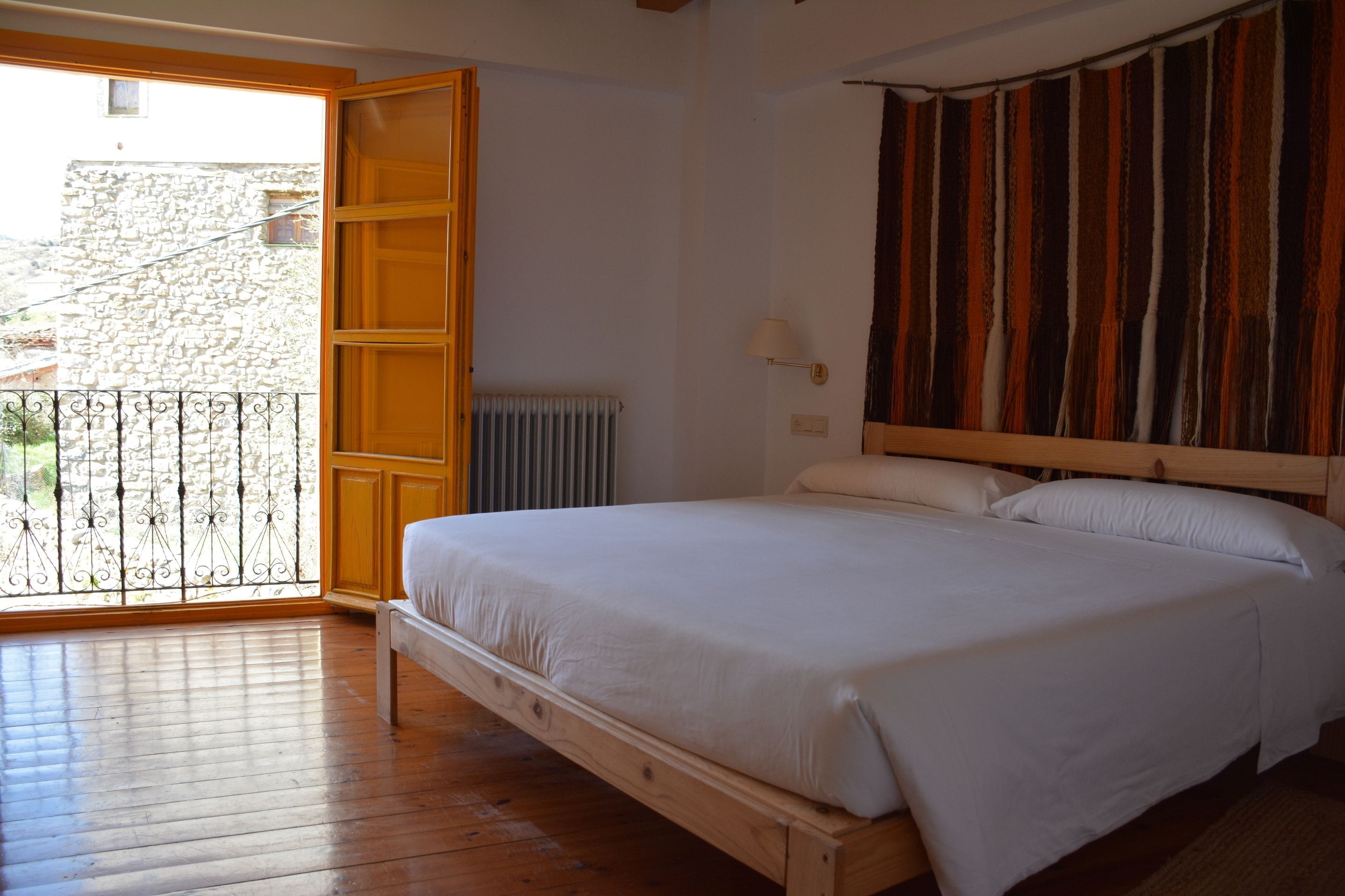 Un dormitorio con cama de madera, vista a un edificio de piedra a través de una puerta abierta y un radiador en la pared.