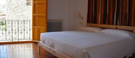 Un dormitorio con cama de madera, vista a un edificio de piedra a través de una puerta abierta y un radiador en la pared.