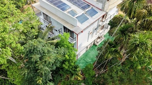 Un immeuble à plusieurs étages, doté de panneaux solaires sur le toit, entouré d’une végétation luxuriante.
