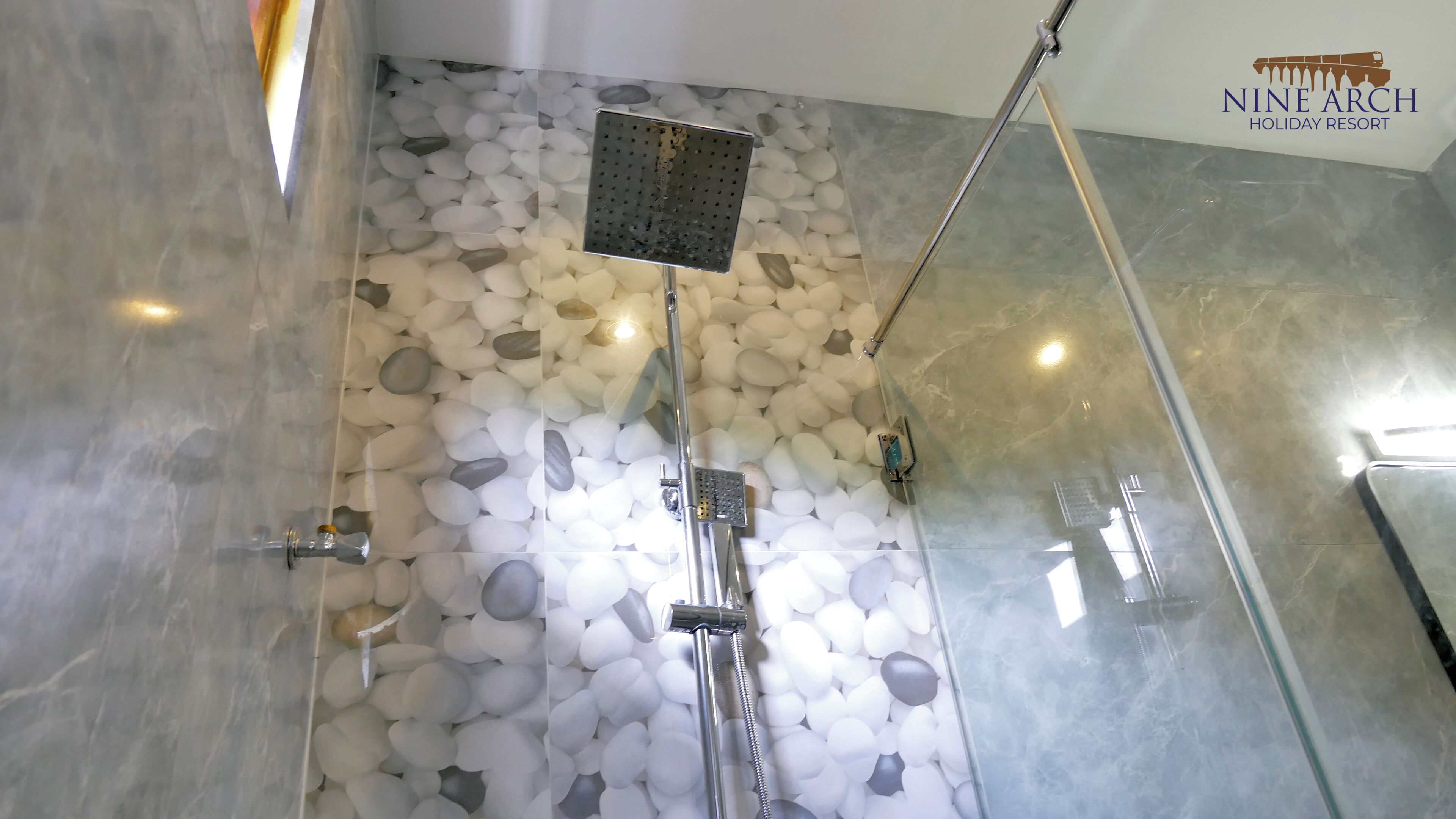 Eine Dusche mit Regendusche und einer Wand aus weißen Kieselsteinen.