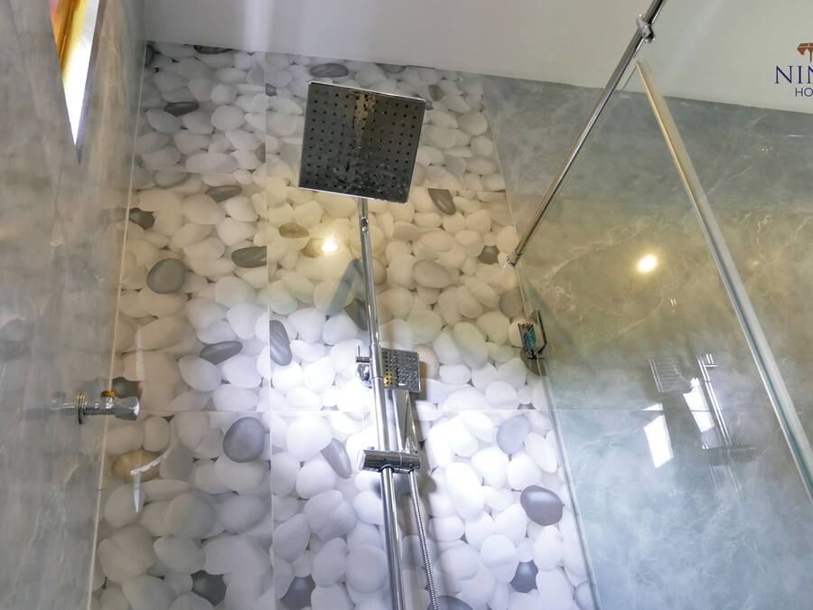 Eine Dusche mit Regendusche und einer Wand aus weißen Kieselsteinen.