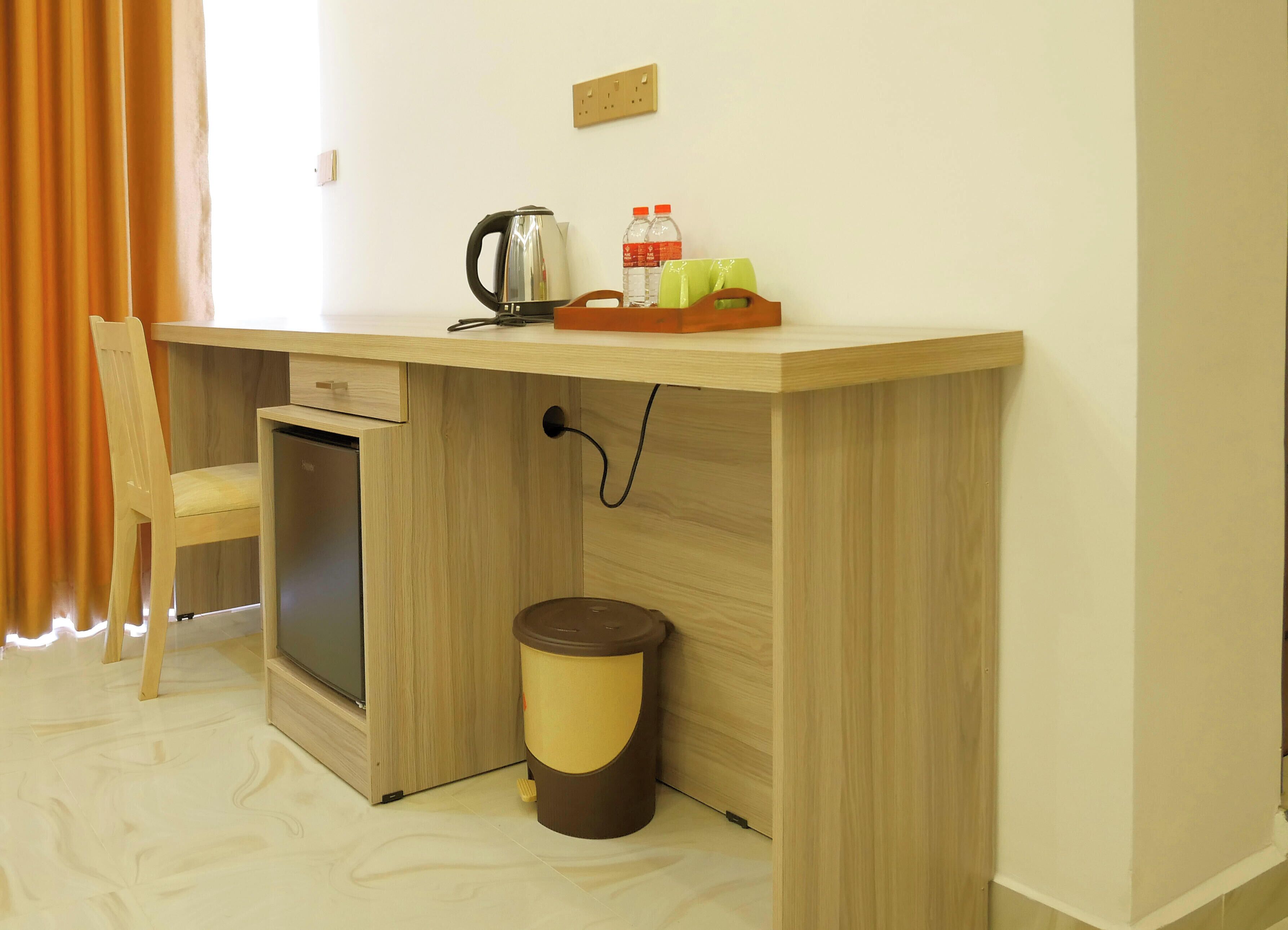 A compact room with a wooden desk, a small refrigerator, a trash bin, and a chair.