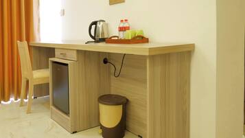 A compact room with a wooden desk, a small refrigerator, a trash bin, and a chair.
