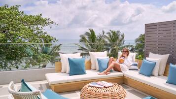 A balcony with a sofa and chairs, overlooking a beach and palm trees.