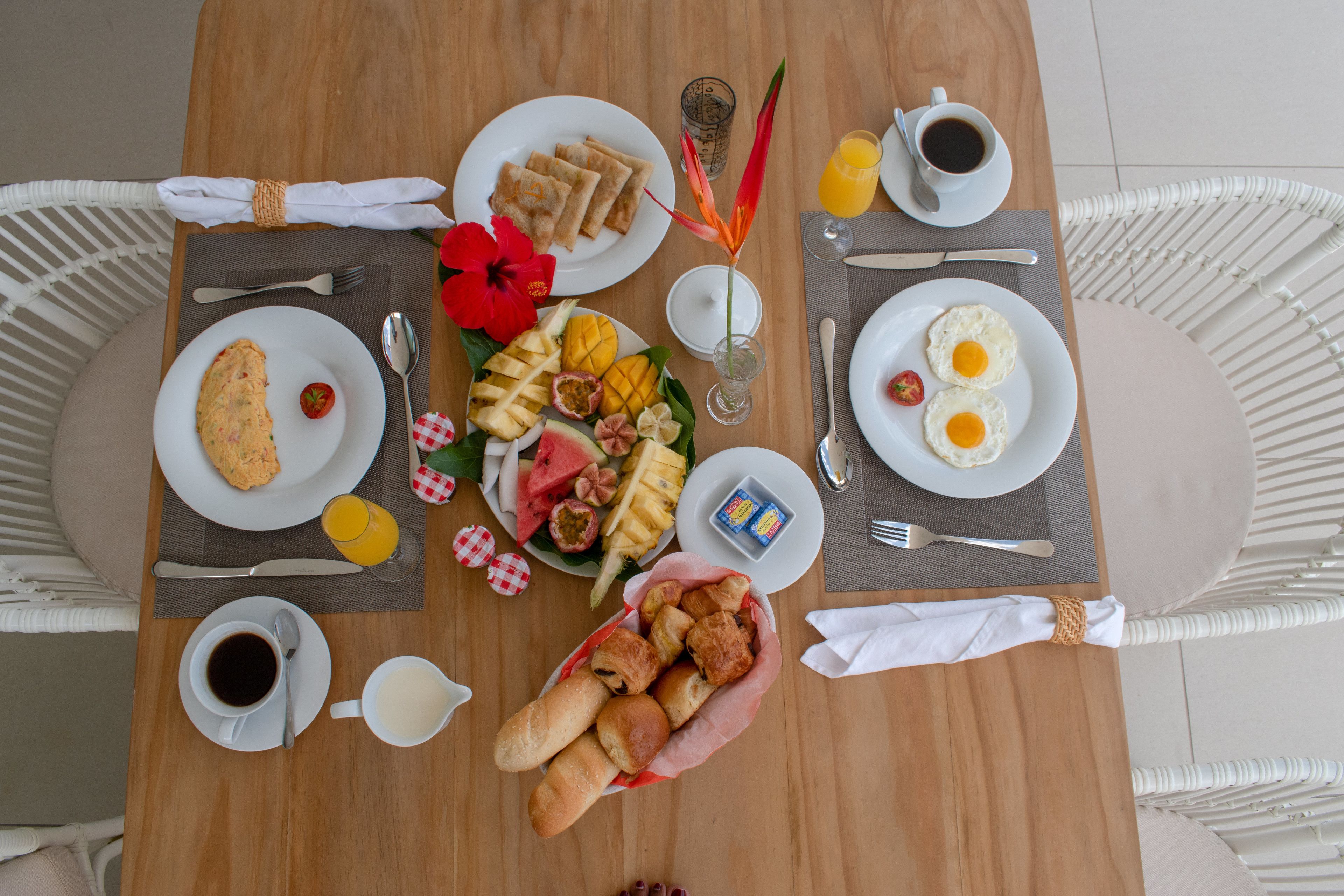 A breakfast table with plates of food, cups of coffee, and a fruit basket.