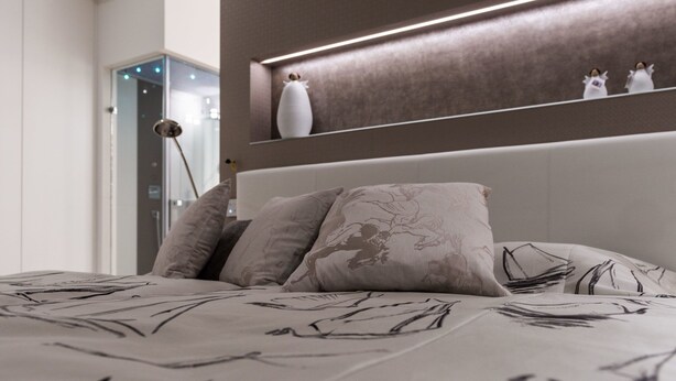 Un dormitorio moderno con una cama grande, un cabecero con iluminación integrada y una mesita de noche con objetos decorativos.
