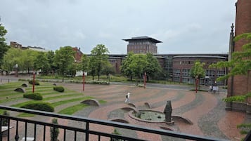 A courtyard with a statue, brick pathways, and a building with a tower in the background.