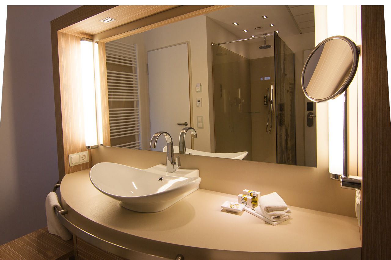 Een moderne badkamer met een groot ovaal wastafel, een spiegel en een douche met glazen wanden.