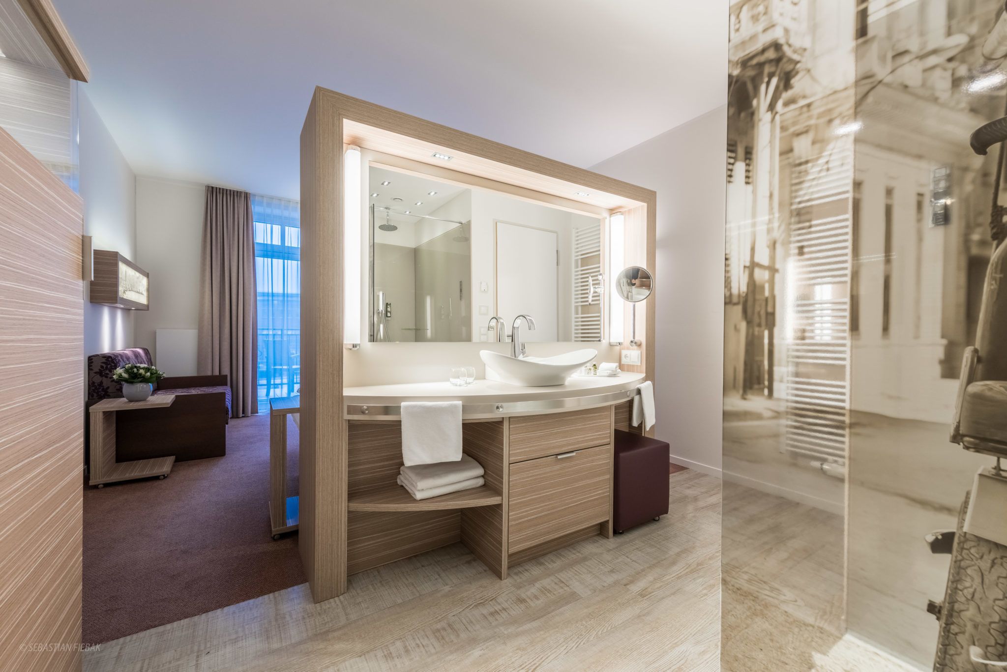 Un baño moderno con un espejo grande, tocador de madera y cabina de ducha con mampara de vidrio.