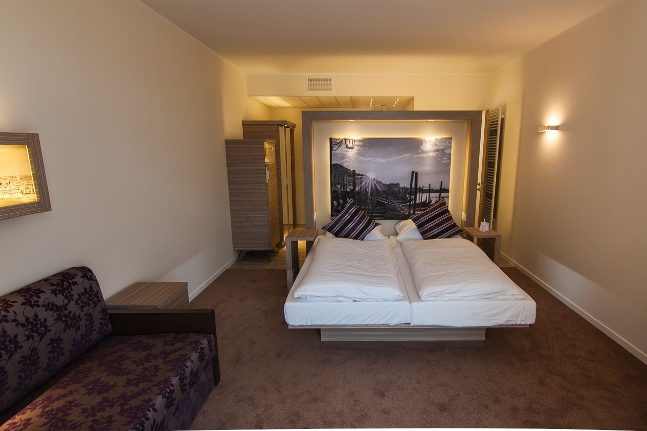 Una habitación de hotel con cama, sofá, armario y un cuadro en la pared.