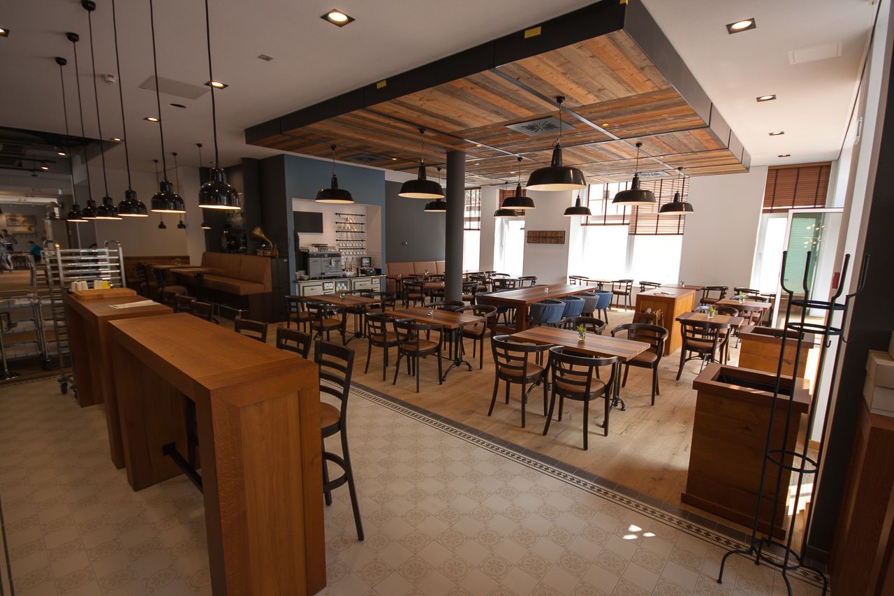 Un café amplio con mesas y sillas de madera, una zona de bar e iluminación colgante.