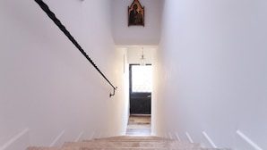 Un escalier étroit, doté d’une rampe en bois, mène à une porte située en haut, qui donne sur une pièce avec une fenêtre.