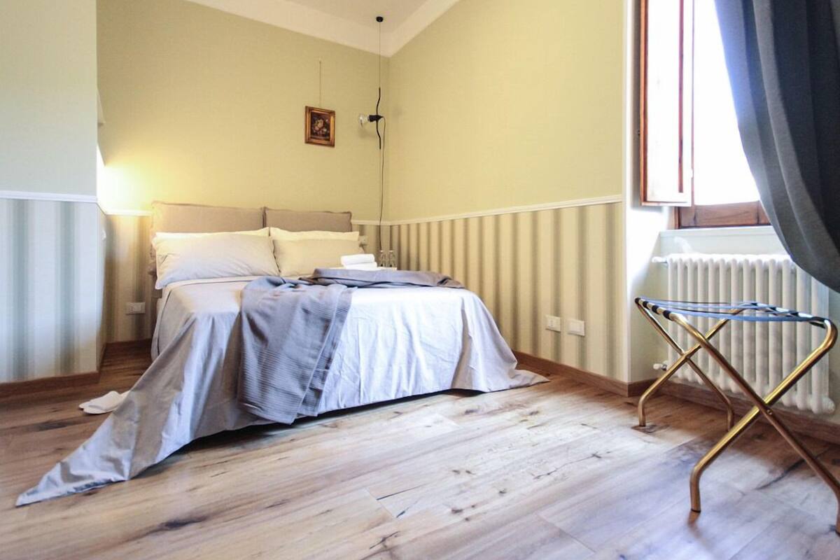Een slaapkamer met een bed, een radiator en een raam met gordijnen.