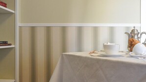 Un coin repas avec une table dressée pour deux personnes, une nappe blanche et une théière en argent.