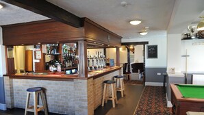 Una zona de bar con taburetes, mesa de billar y mesa de futbolín.