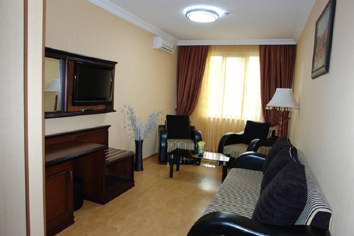 Ein Wohnzimmer mit einer Couch, Sesseln, einem Couchtisch, einem Fernseher und einer Lampe.
