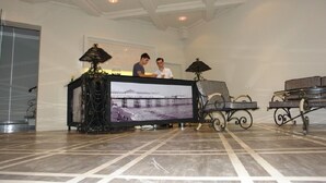 A reception area with a reception desk, two staff members, a large framed photograph, and decorative lamps. - Hotel Brighton (Batumi)