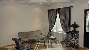 A room with a sofa, a small table, a lamp, and a window with curtains. - Hotel Brighton (Batumi)