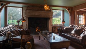 A cozy living room with a fireplace, leather sofas, wooden furniture, and large windows offering a view of the outdoors. - Hotel Spa Les Pins De César (Saint-Jouin-Bruneval)