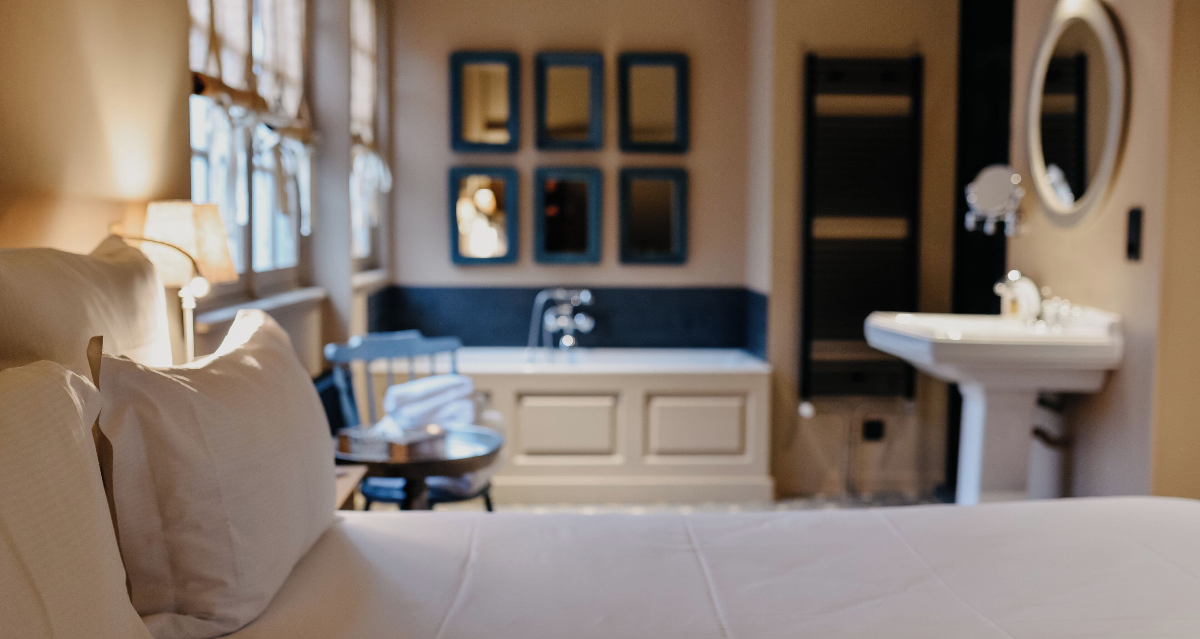 A hotel room with a bed, a desk, a chair, a sink, and a mirror.