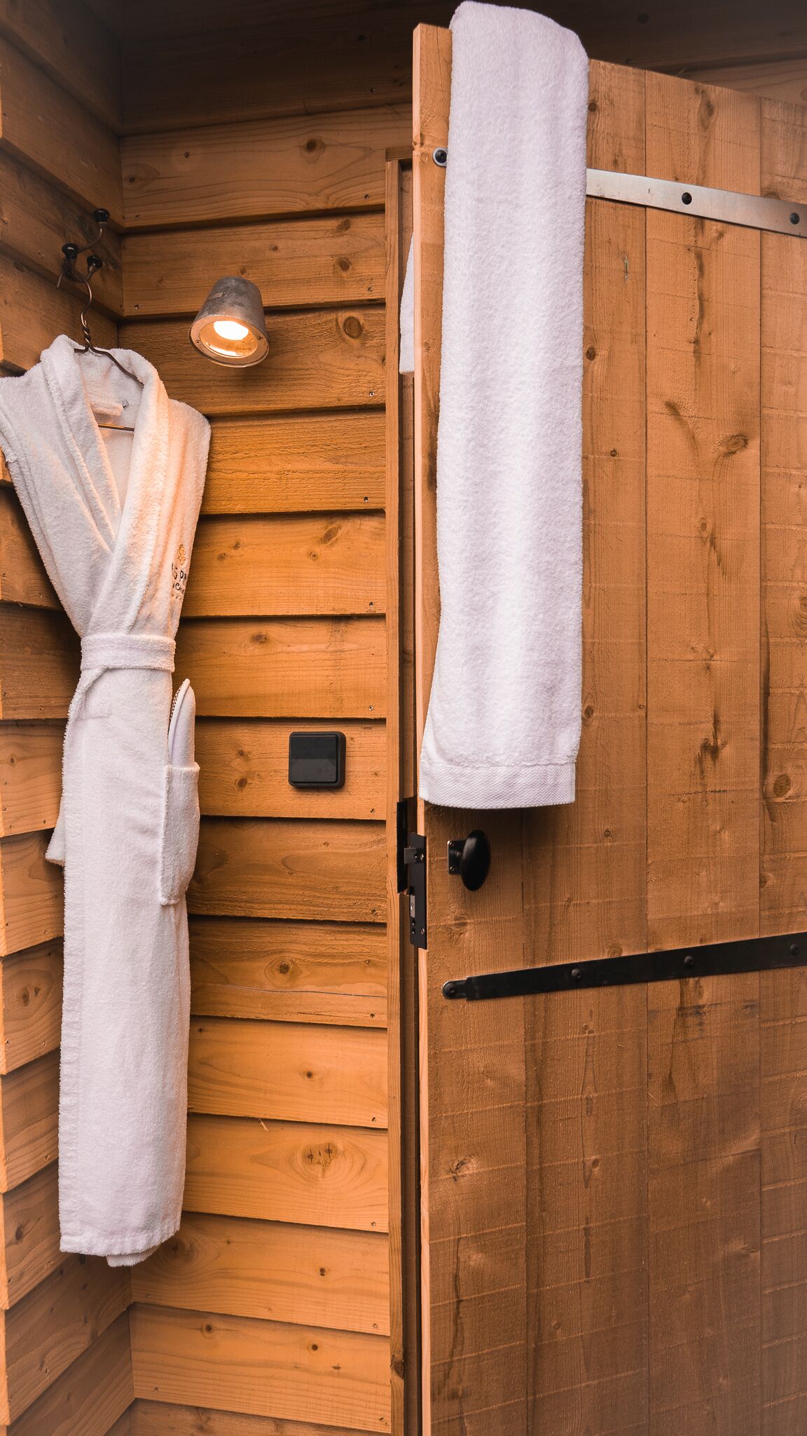A wooden cabin with a sauna room. There is a white towel hanging on the wall and another on the door.