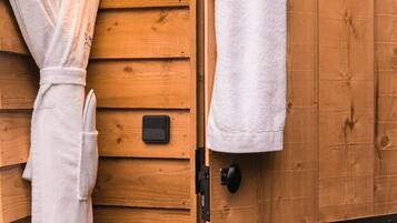 A wooden cabin with a sauna room. There is a white towel hanging on the wall and another on the door.