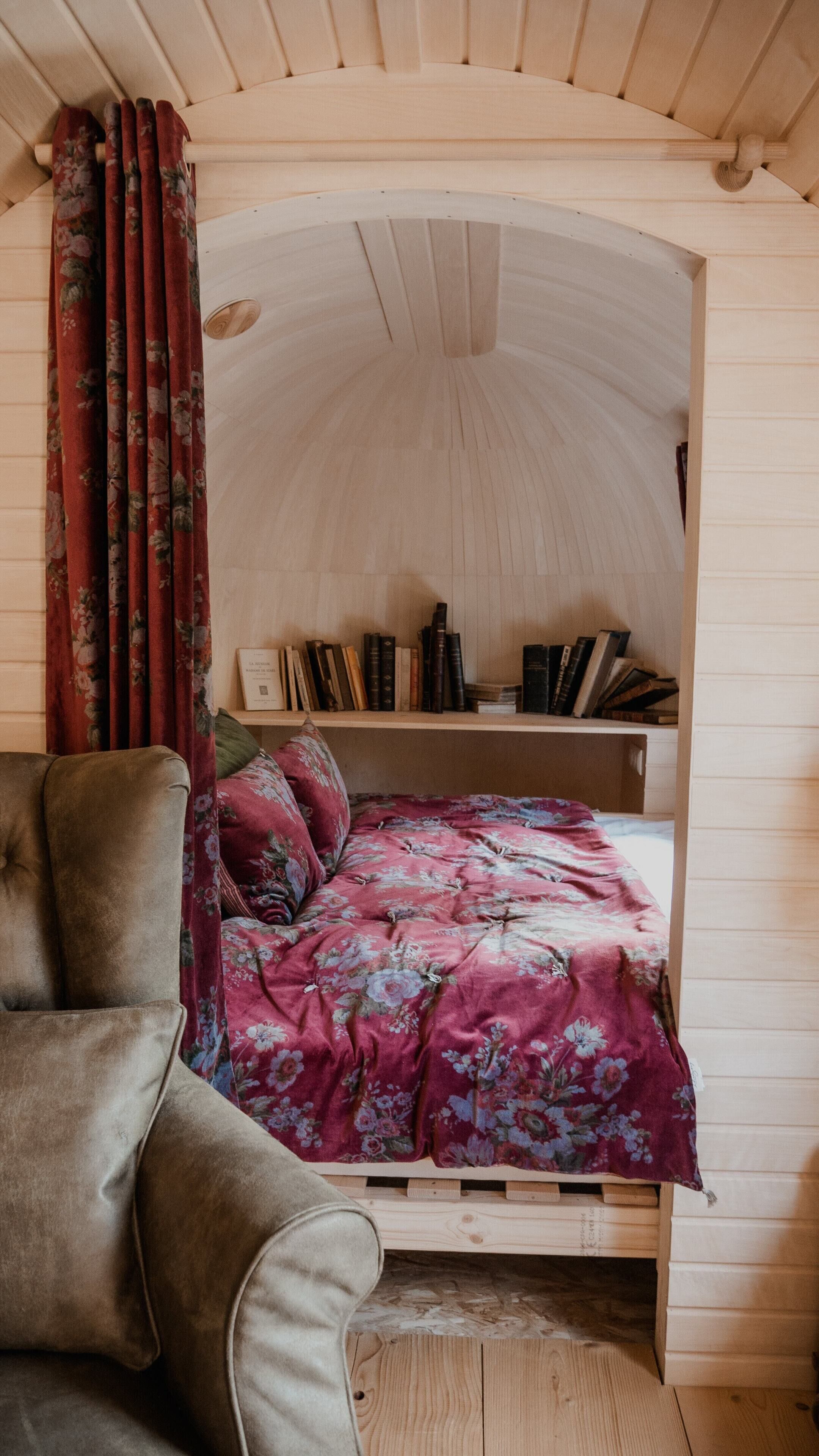 A cozy room with a wooden bunk bed, a plush armchair, and a bookshelf filled with books.