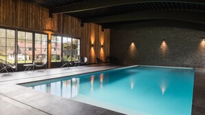 An indoor swimming pool with clear glass walls, wooden paneling, and modern lighting. - Hotel Spa Les Pins De César (Saint-Jouin-Bruneval)