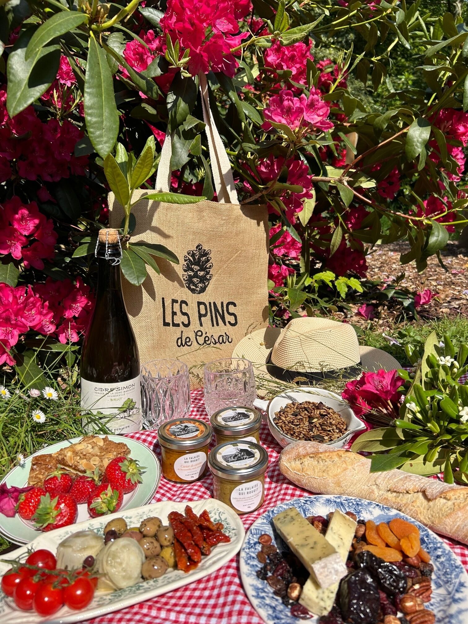 A picnic setup with a bottle of wine, a basket, and various food items on a checkered tablecloth.