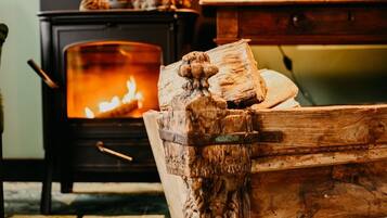 Une pièce chaleureuse avec un poêle à bois, une coffre en bois sculpté et une table avec une lampe.
