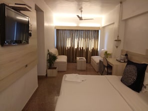 A hotel room with a bed, a desk, a chair, a TV, and a ceiling fan. - Hotel Samraj (Mumbai)