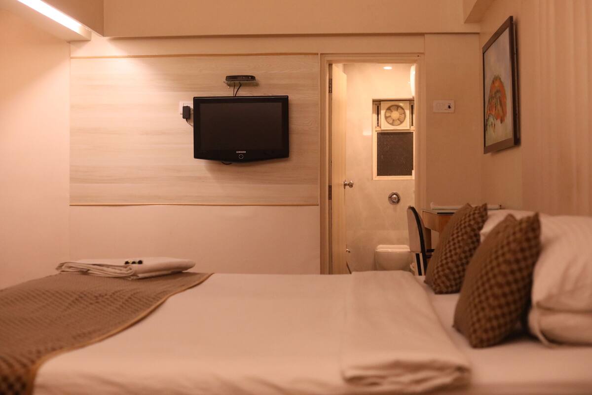 A hotel room with a bed, a television mounted on the wall, a door leading to a bathroom, and a framed picture on the wall.