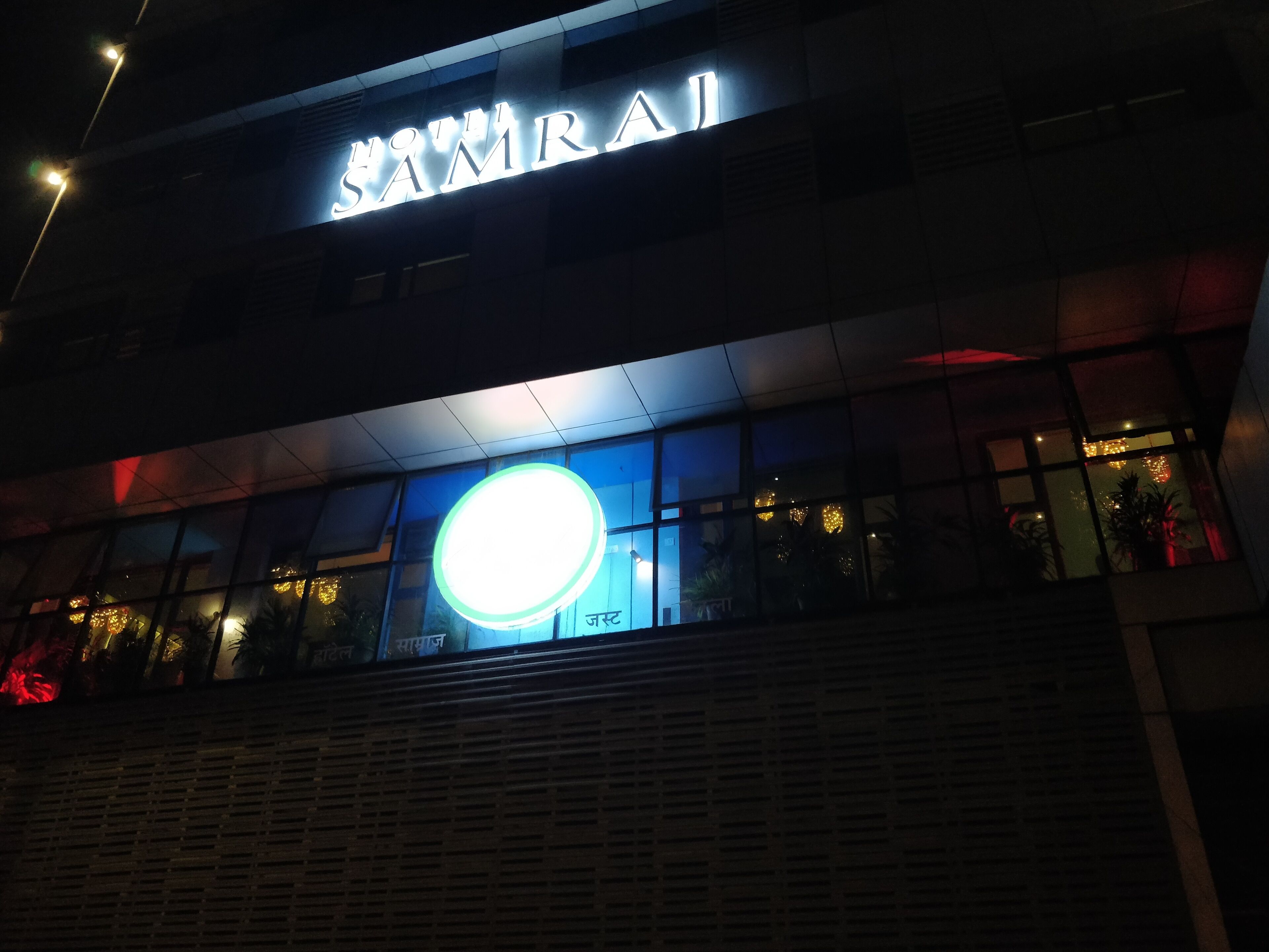 A building with a sign that reads "SAMRAJ" and a large illuminated circular sign below it.