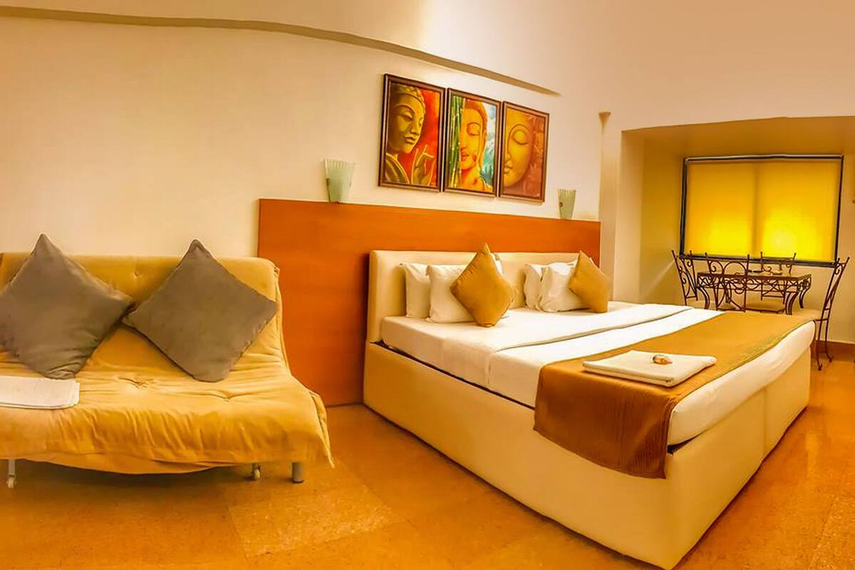 A hotel room with a bed, a sofa, and a table with a lamp.