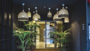 A hallway with multiple hanging pendant lights, potted plants, and a glass door leading to a room.