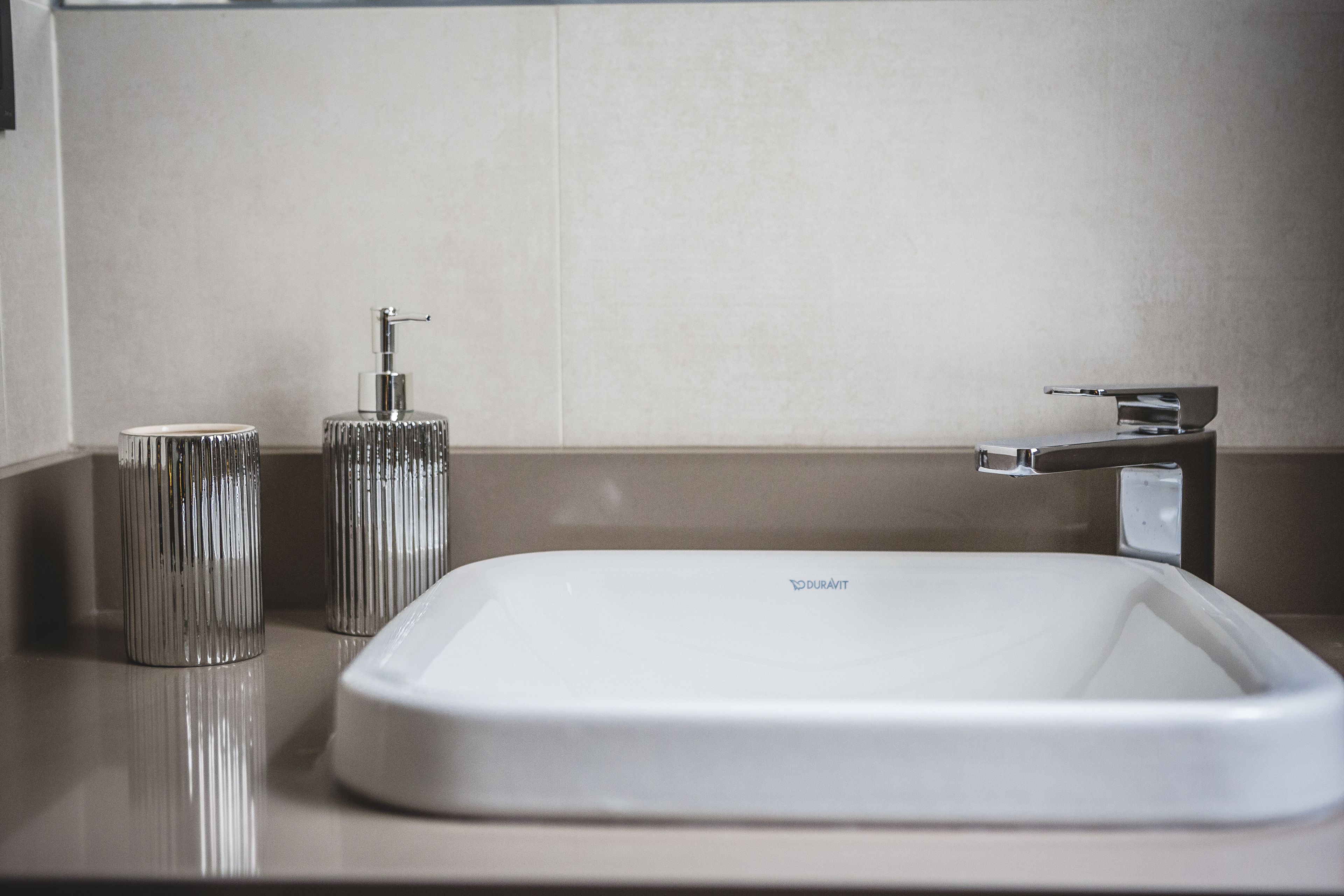 Un baño moderno con un lavamanos blanco, un grifo de cromo y un dispensador de jabón cilíndrico.