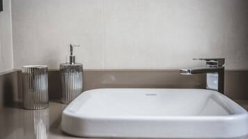 A modern bathroom with a white sink, a chrome faucet, and a cylindrical soap dispenser.