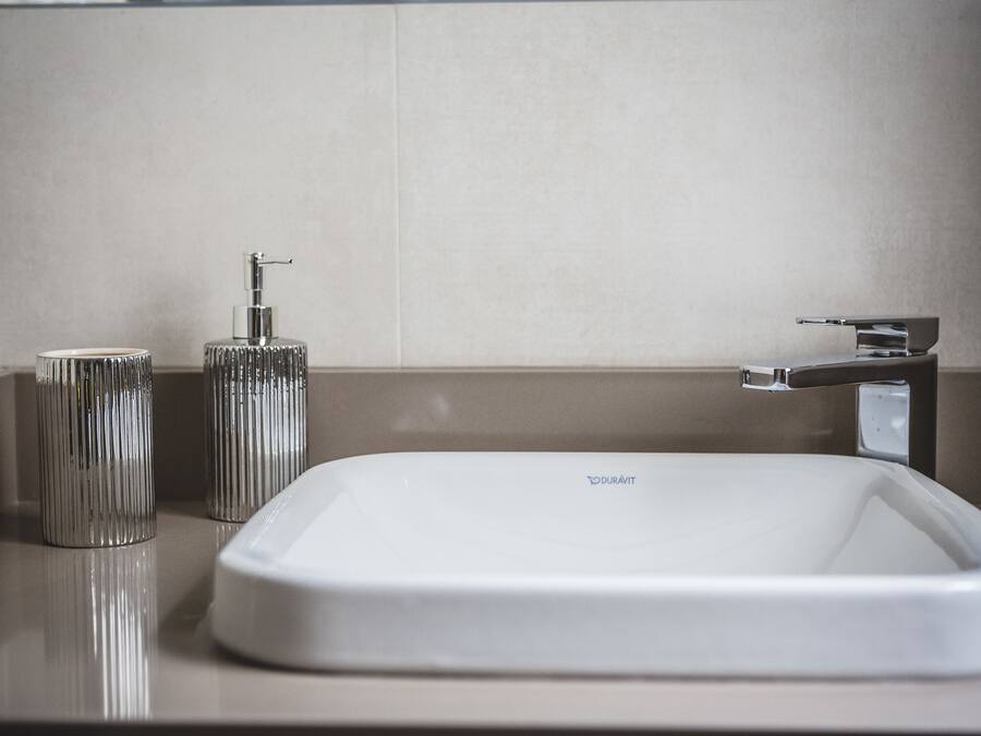 A modern bathroom with a white sink, a chrome faucet, and a cylindrical soap dispenser.